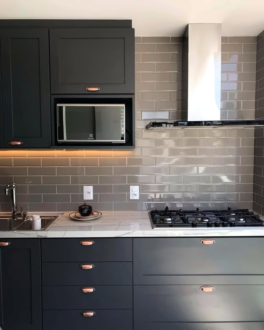 Cozinha com armários grafite, azulejo metrô, coifa inox e cooktop