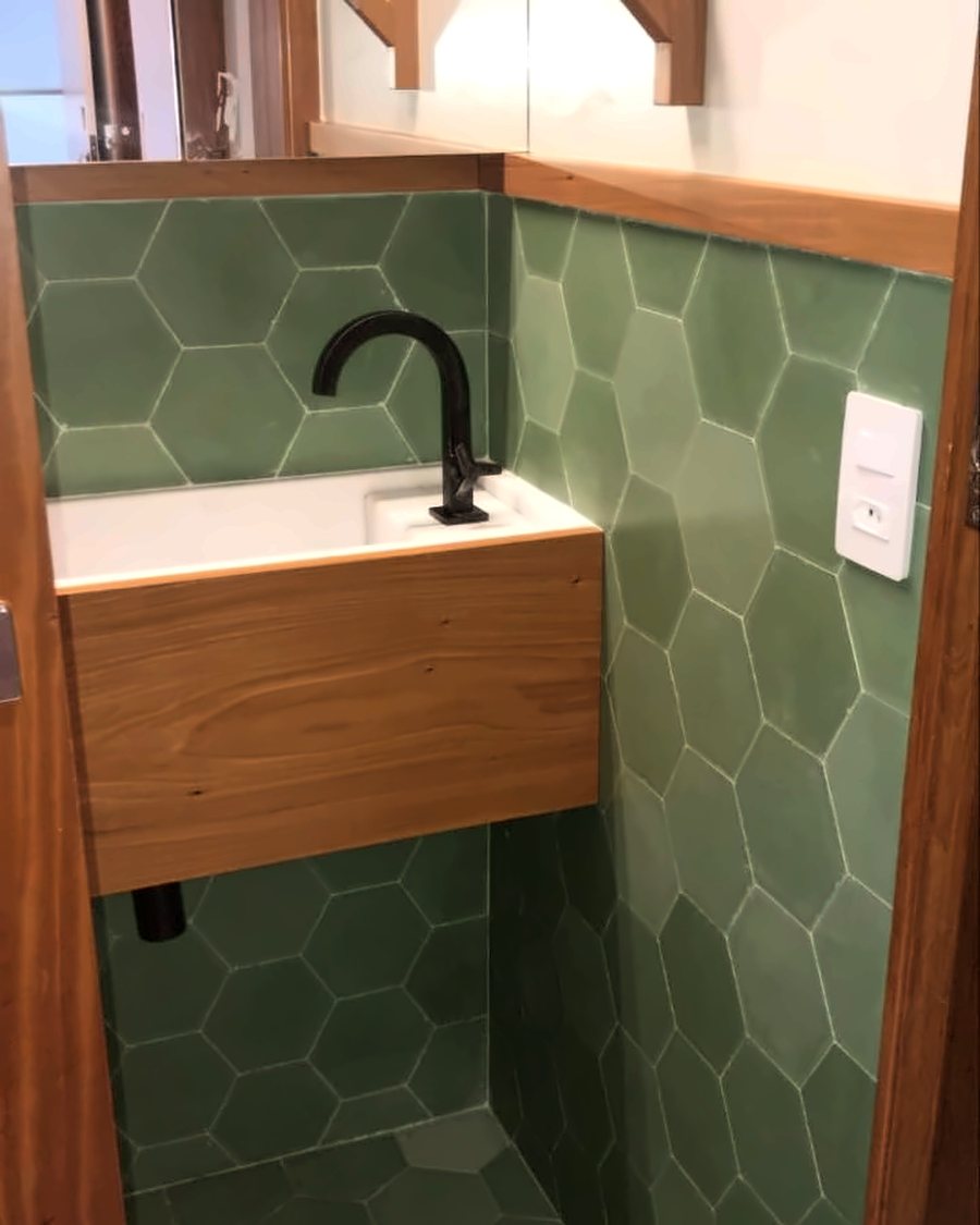 Lavabo com revestimento hexagonal verde, torneira preta e marcenaria em madeira