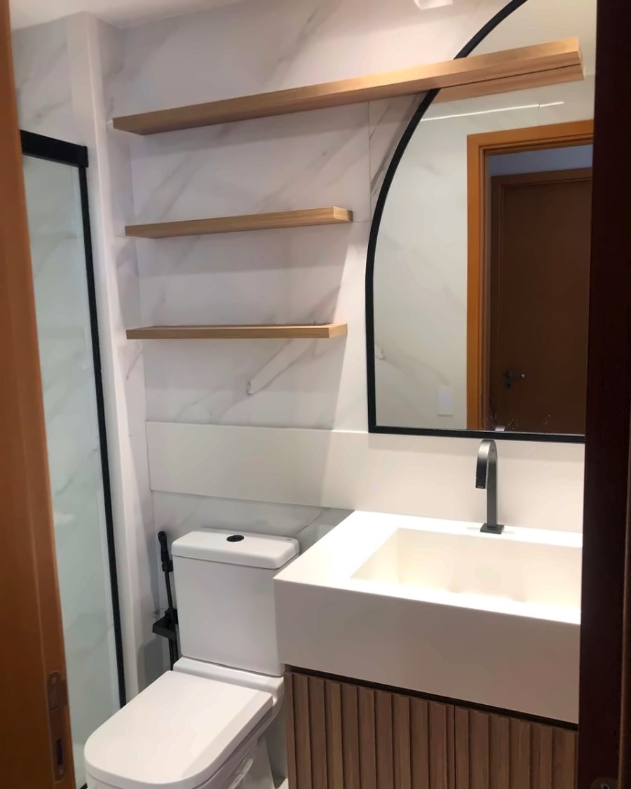 Lavabo revestido em mármore com cuba esculpida, espelho arqueado e prateleiras de madeira