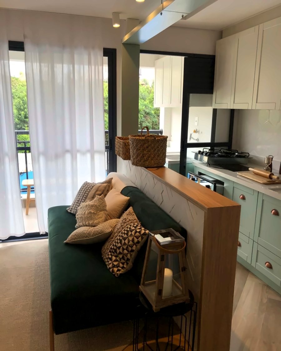 Sala de estar integrada à cozinha, com sofá verde e bancada de madeira